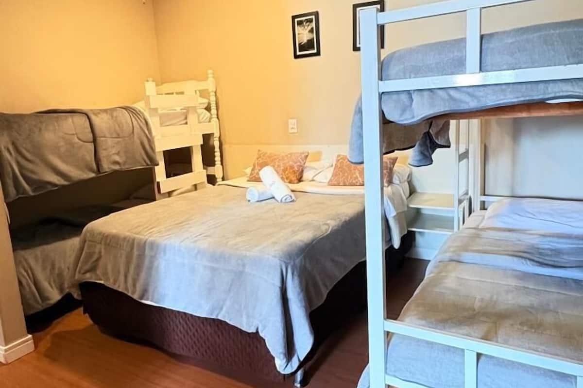 A dormitory room with two bunk beds, wooden flooring, and a ceiling light.