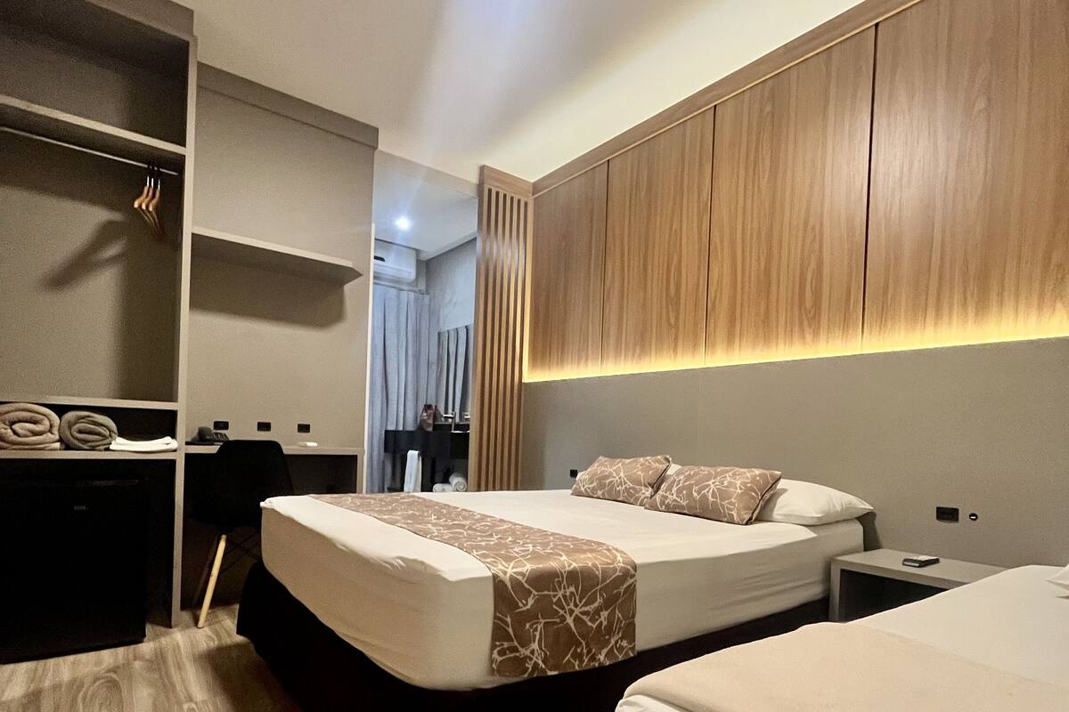 A modern hotel room with two beds, a desk, and a wardrobe.