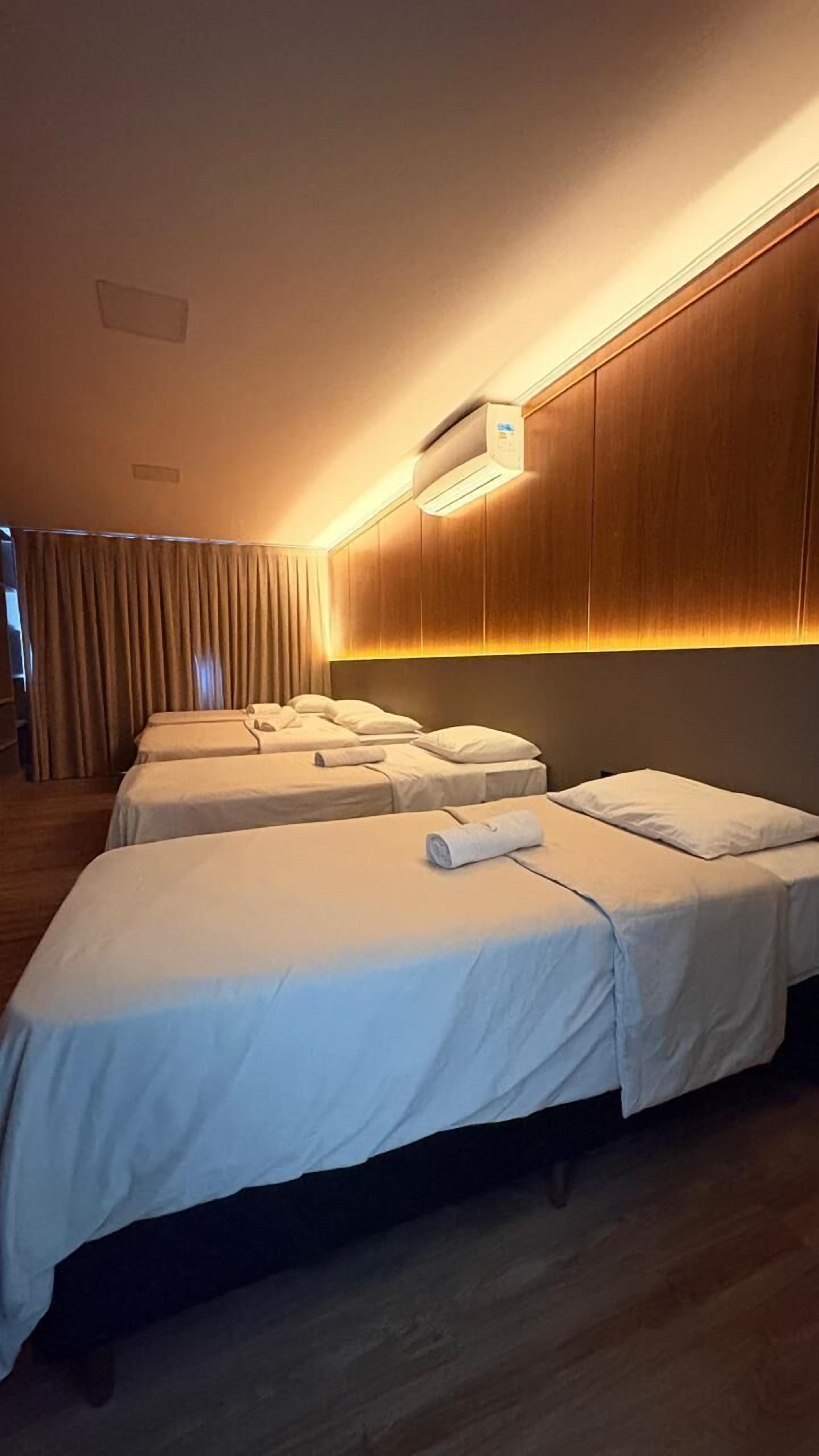 Habitación de hotel con tres camas, paneles de madera en las paredes y un equipo de aire acondicionado sobre las camas.