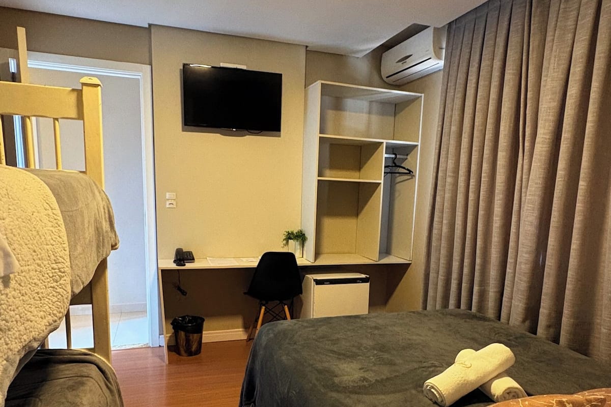 A hotel room with two beds, a desk, a television, an air conditioning unit, and a wardrobe.