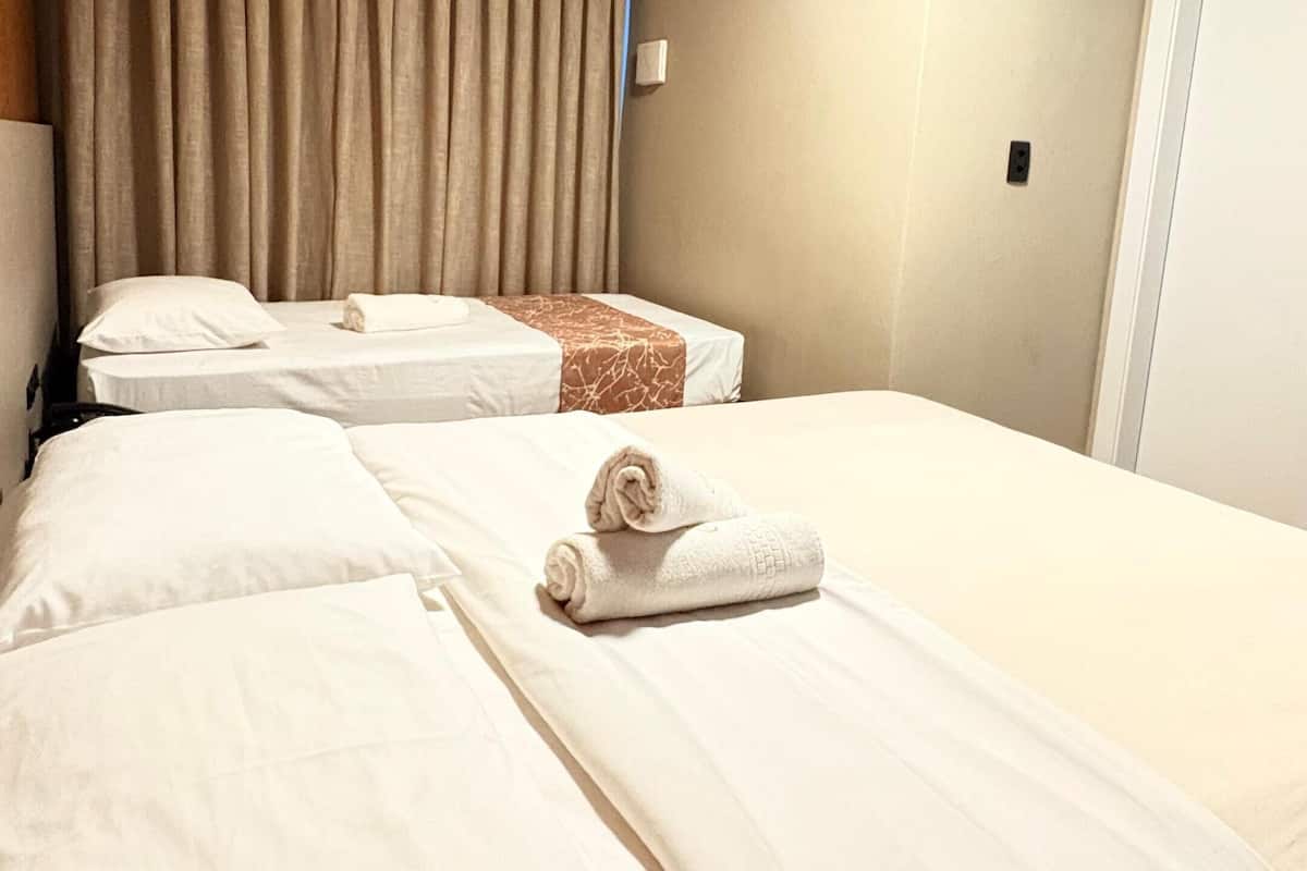 A hotel room with two beds, beige walls, a window with curtains, and a door.