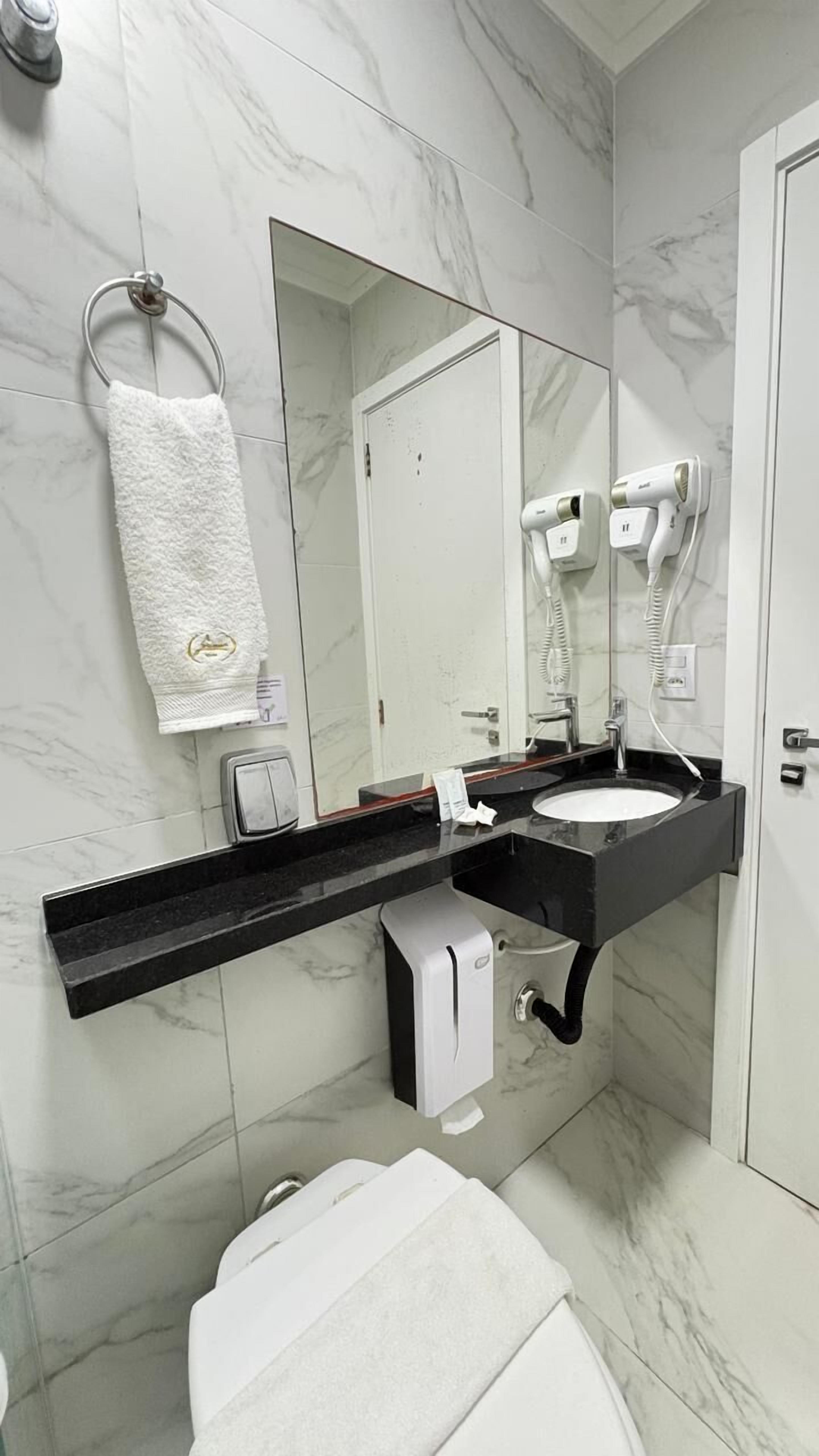 A modern bathroom with a marble floor, a black countertop sink, a white towel, a hand dryer, and a soap dispenser.