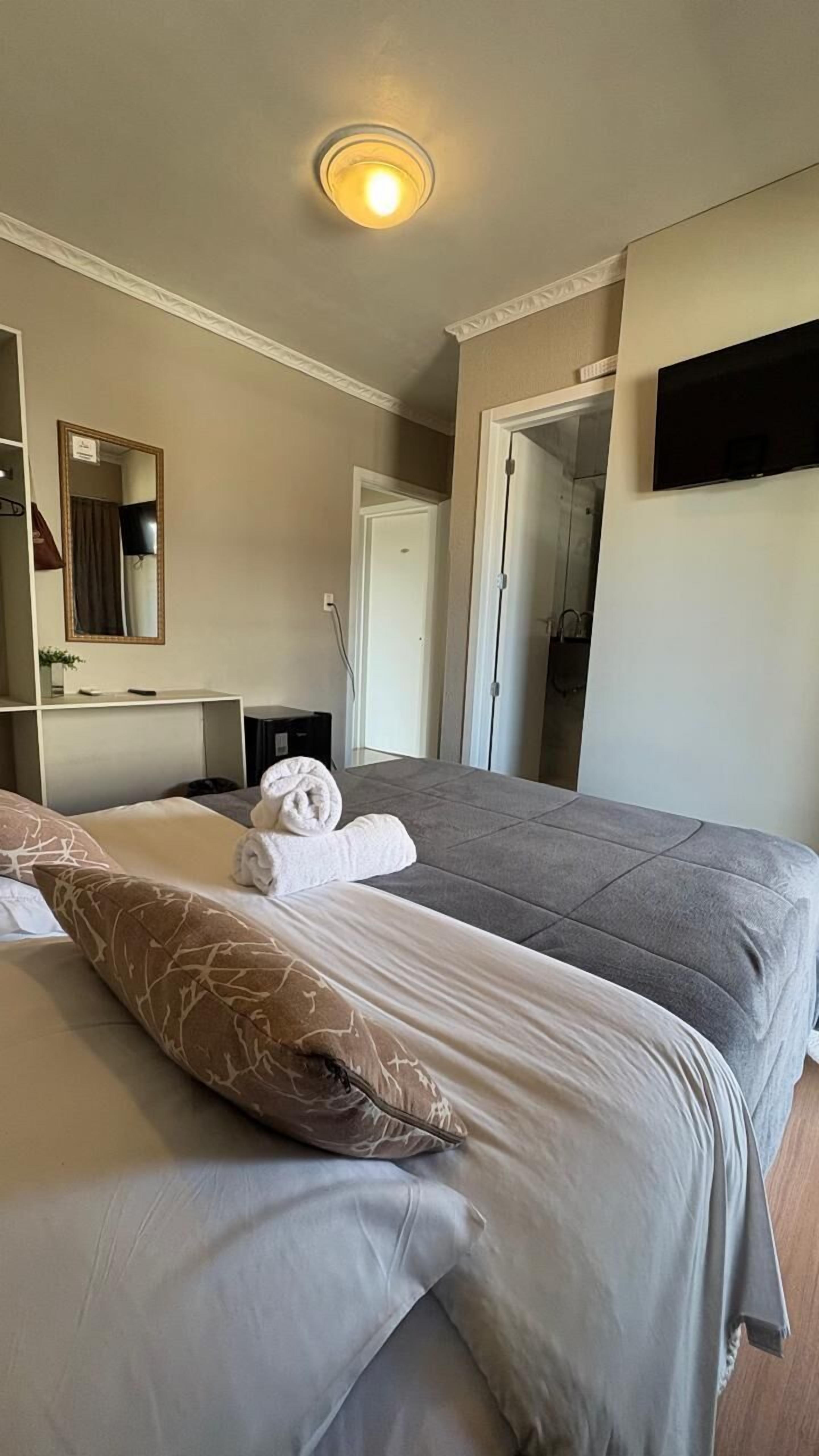 Una habitación de hotel con dos camas, un televisor de pantalla plana, un espejo y una lámpara en el techo.