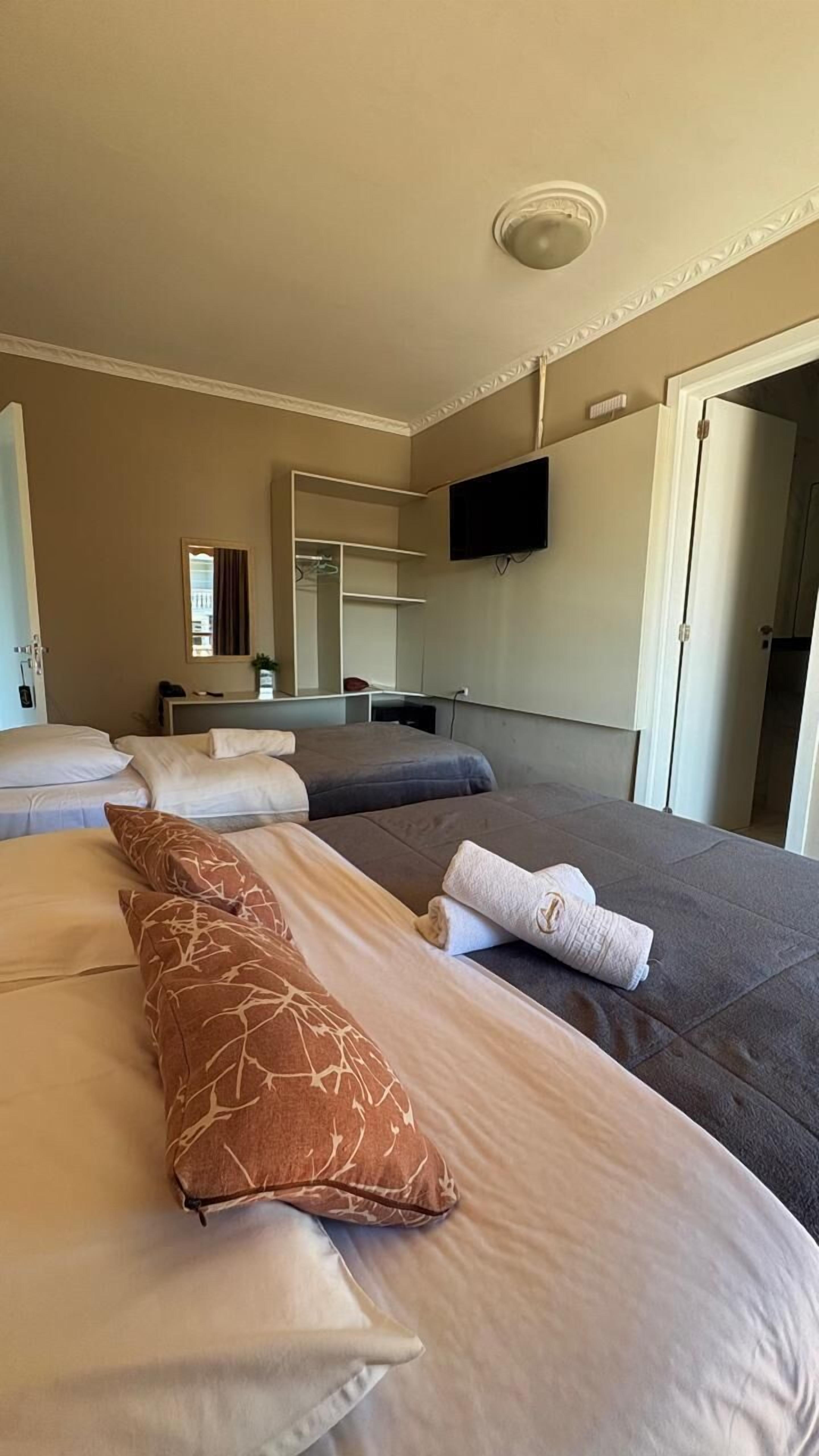 Quarto de hotel com duas camas, televisão de tela plana na parede e espelho sobre a cama.