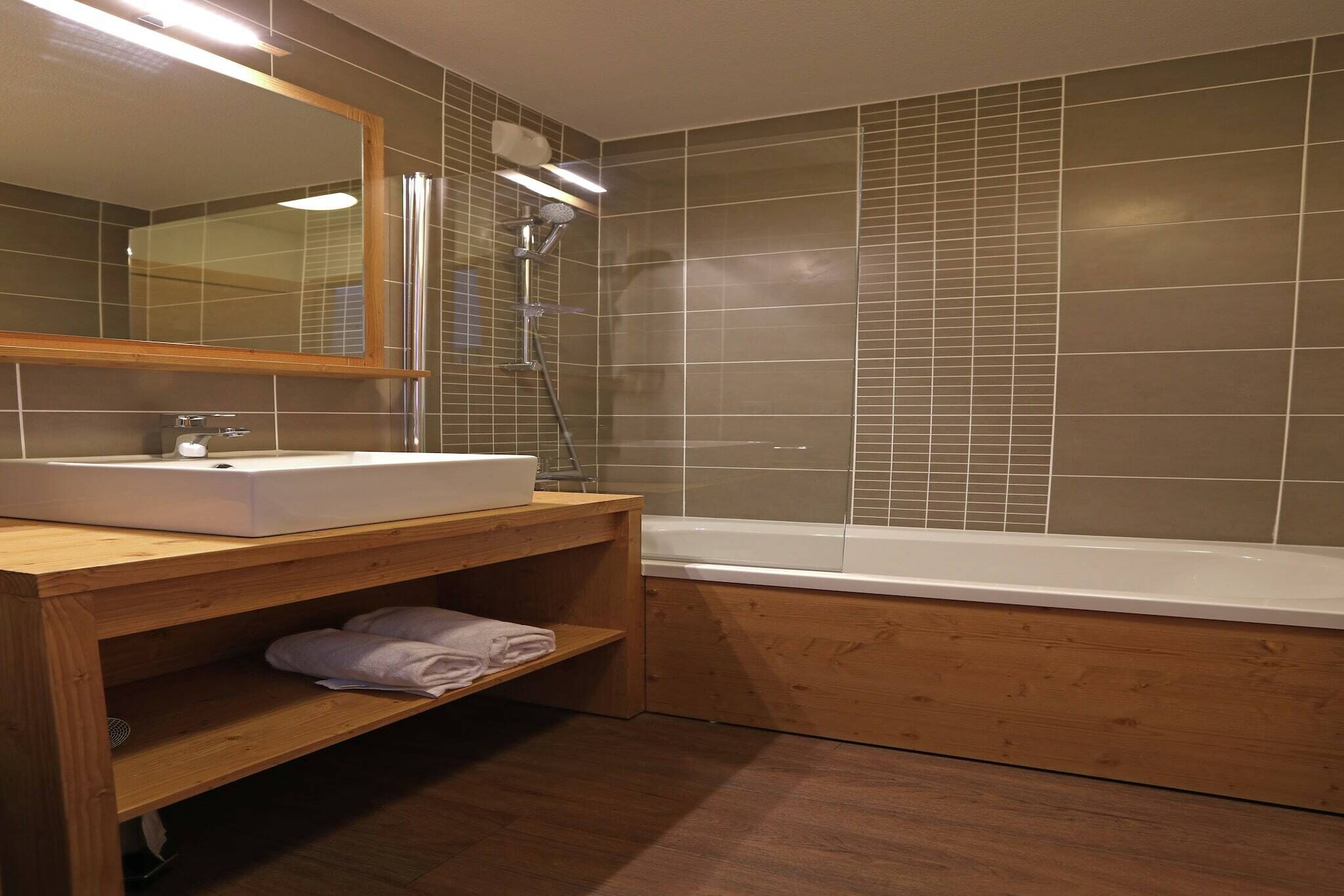 A modern bathroom with a wooden vanity, a large mirror, a white sink, and a bathtub.