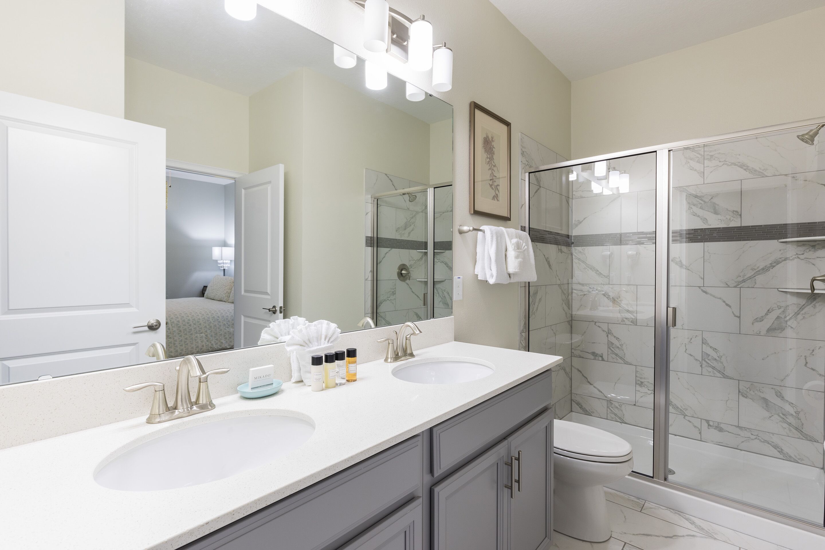 A modern bathroom with two sinks, a large mirror, and a glass-enclosed shower.
