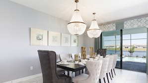 Un espace repas avec une table en bois foncé, des chaises à revêtement blanc et des lustres en cristal.