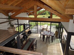 Ein geräumiger Essbereich mit Holztisch und Stühlen, eine Küchenzeile mit Spüle und Schränken sowie Blick auf ein grünes Feld durch große Fenster.