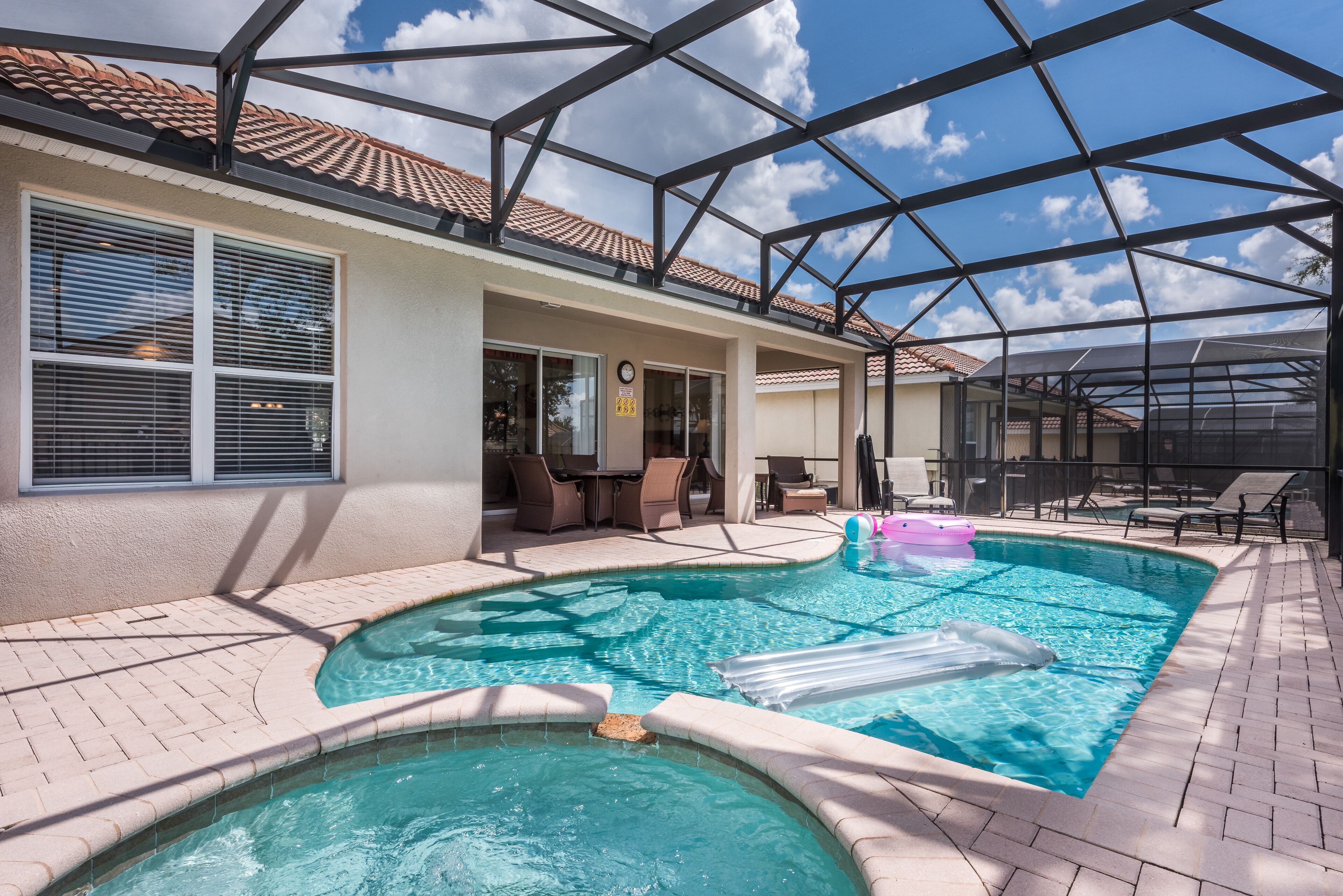 A pool area with a hot tub, lounge chairs, and a covered patio.