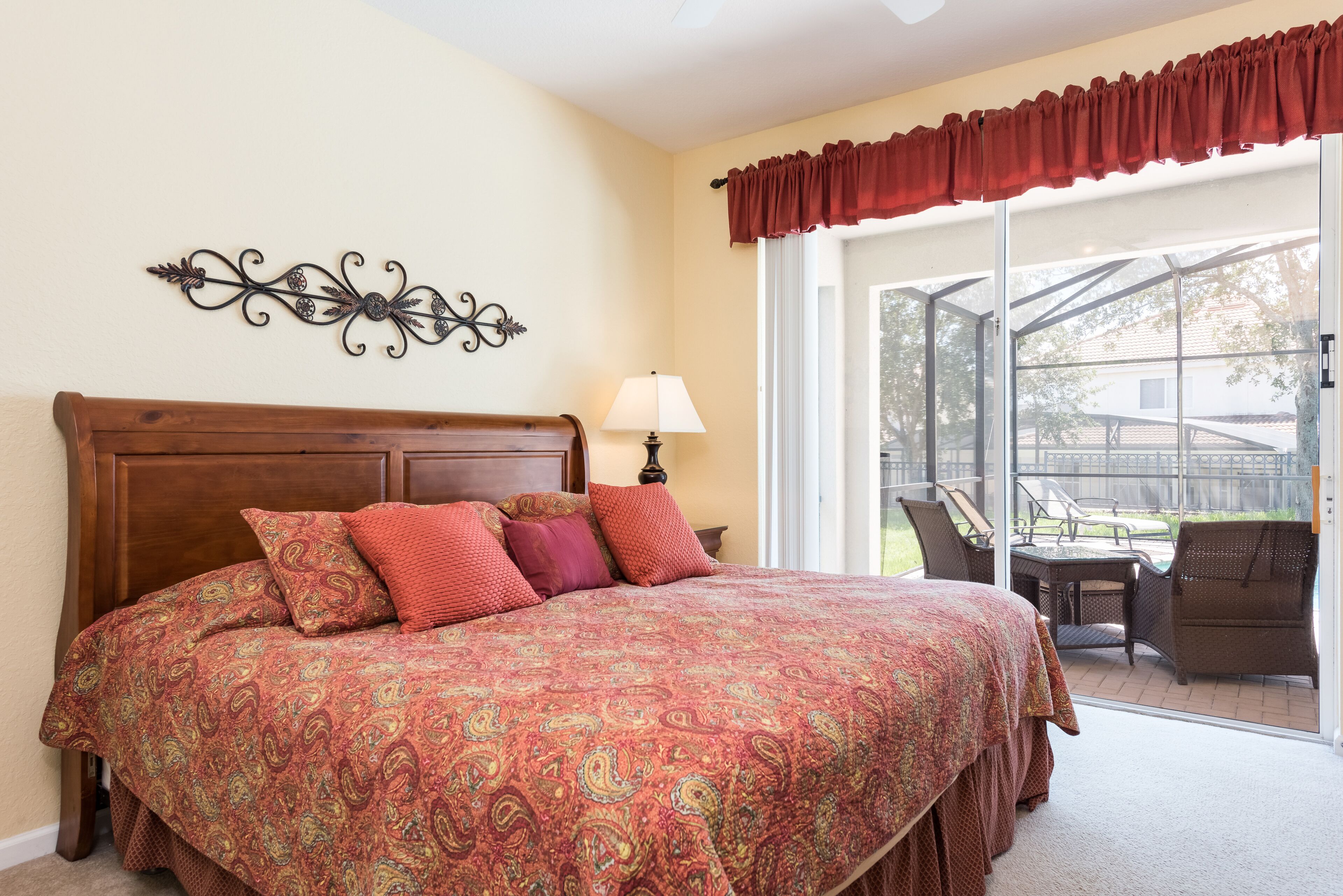 A bedroom with a large bed, a nightstand, a lamp, and a view of an outdoor patio.