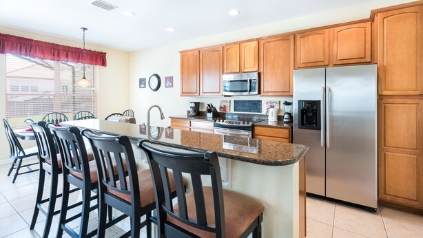 A kitchen with wooden cabinets, a stainless steel refrigerator, a microwave, and a large island with bar stools. - Kissimmee Resort Villa, 4 Bed / 4 Bath En-Suite, Heated South Pool & AC Arcade (Kissimmee)