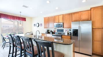 A kitchen with wooden cabinets, a stainless steel refrigerator, a microwave, and a large island with bar stools.