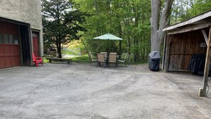 Um estacionamento de cascalho com uma garagem vermelha, uma mesa de piquenique coberta e um galpão de madeira.