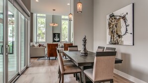 Un espace repas comprenant une longue table, six chaises et des luminaires suspendus.