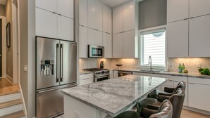 Une cuisine moderne dotée d’appareils électroménagers en acier inoxydable, d’un îlot en marbre et d’un coin salon avec des fauteuils en cuir.