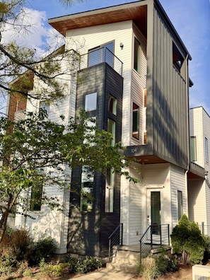 A multi-story residential building with a modern architectural design, featuring a combination of white and dark siding, large windows, and a visible front entrance.