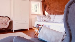 A bedroom with a bed, a white wardrobe, a patterned armchair, and a rustic headboard. - FELSENHAUS with view over Trier - living in the rock (Trier)