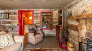 A cozy room with a stone wall, a wooden ceiling, a leather armchair, a bookshelf, and a fireplace. - Stay in a 200 Year Old Log Cabin with Modern Conveniences (Bland)