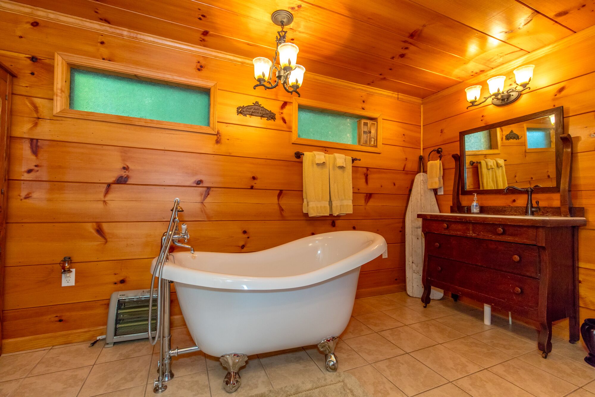 Ein Badezimmer einer Holzhütte mit freistehender Badewanne, einem Holzwaschtisch mit Spiegel und zwei Haken für Handtücher.