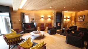 A cozy living room with wooden walls, a fireplace, and a variety of seating options including a sofa, chairs, and a round table. - Apartment on slopes in Les Menuire (les Menuires)