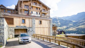 A multi-story wooden building with balconies and a car parked in front. - Apartment on slopes in Les Menuire (les Menuires)