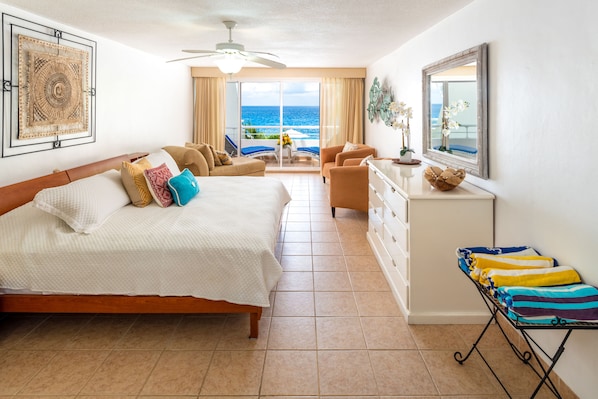 Una camera d'hotel con un letto, una zona salotto con vista sull'oceano, una scrivania con uno specchio e un portasciugamani.