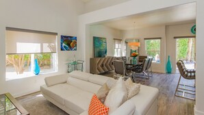 A spacious living room with a white sofa, dining area with chairs, and a large window providing natural light. - Vista View -Fun in the Sun!  Just minutes from  Downtown Palm Springs and  Tram (Palm Springs)