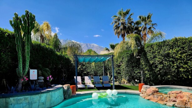 A pool with clear blue water, surrounded by rocks and plants. There are lounge chairs and a pergola with a blue canopy. - Vista View -Fun in the Sun!  Just minutes from  Downtown Palm Springs and  Tram (Palm Springs)