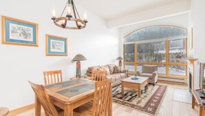 A spacious living room with a wooden dining table, two sofas, a coffee table, and a large window offering a view of a snowy landscape. - 1546 | Wonderful View, Pool & Spa On Keystone Lake (Keystone)