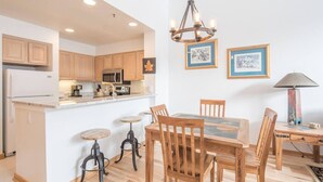 A modern kitchen with wooden cabinets, a central island with stools, a dining table with chairs, and a chandelier. - 1546 | Wonderful View, Pool & Spa On Keystone Lake (Keystone)