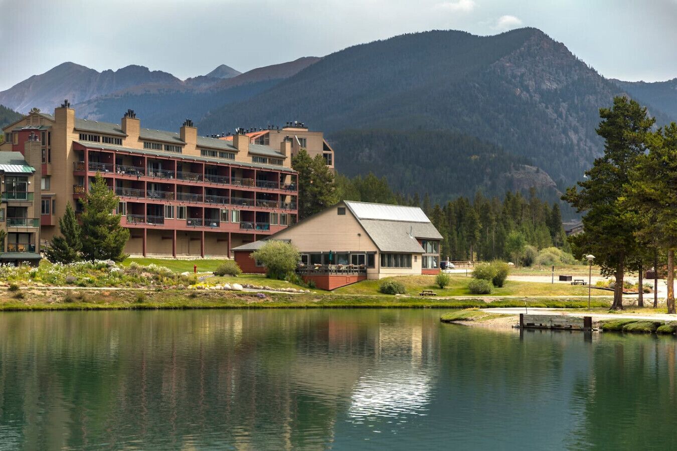 Un hotel con un edificio grande y una estructura más pequeña, ambos con balcones, frente a un paisaje montañoso.