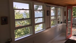 Habitación con amplios ventanales que dan a una masa de agua, techo de madera y puerta que conduce al exterior.