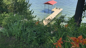 Un muelle de madera se adentra en un lago, rodeado de abundante vegetación y un pabellón de techo rojo.