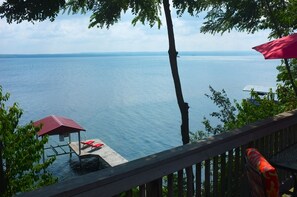 A lakeside view with a wooden deck, red lounge chairs, and a small pavilion. - Cozy Cabin With 165 Ft Beach in the heart of FLX wine country! ALL are welcome! (Penn Yan)