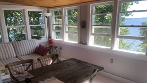 Una habitación acogedora con una mesa de madera, un sofá a rayas y grandes ventanales con vistas a un cuerpo de agua.