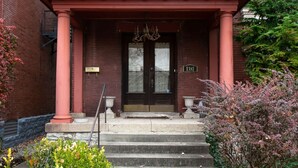 A red brick building with a black double door, a small porch with pink columns, and a number '1381' sign. - Beautiful Victorian Louisville Home (Louisville)