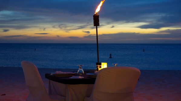 A table set for two with a candle and a bottle, overlooking the ocean at sunset.