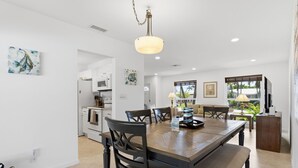 Una cocina moderna con armarios blancos, una mesa de comedor de madera y una lámpara colgante.