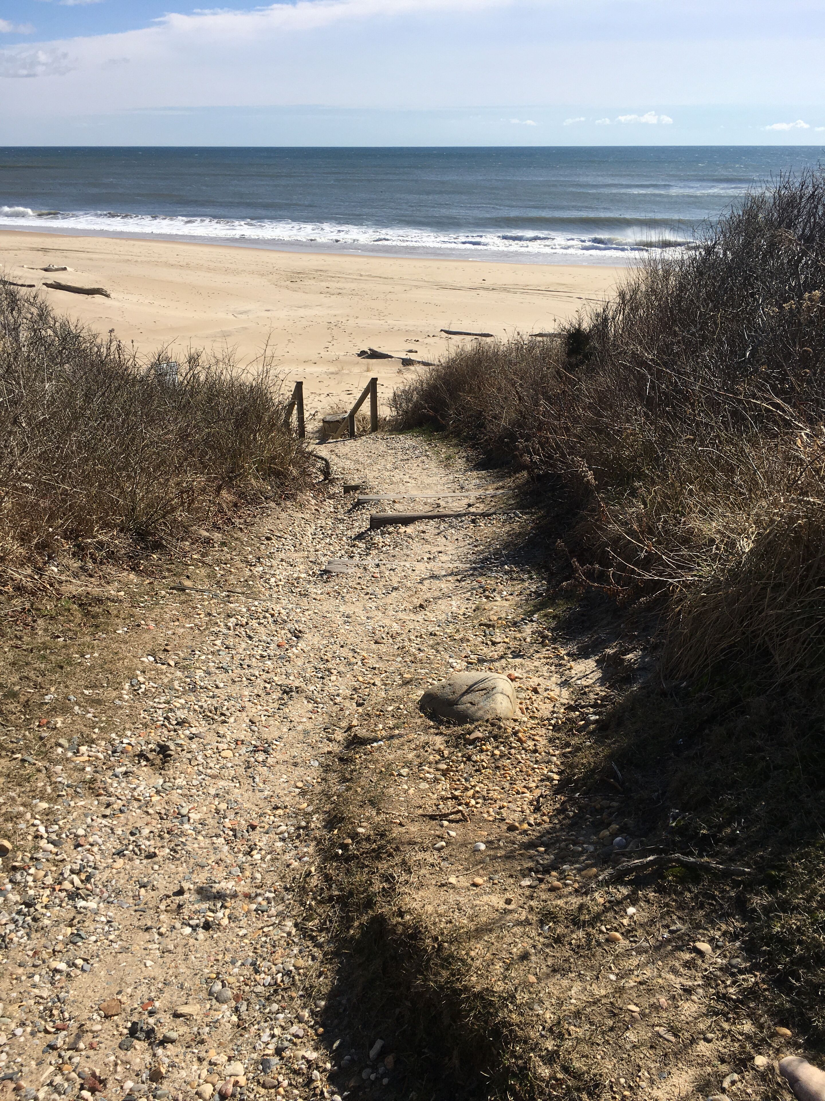 Un sentier de gravier mène à une plage de sable offrant une vue sur l’océan.