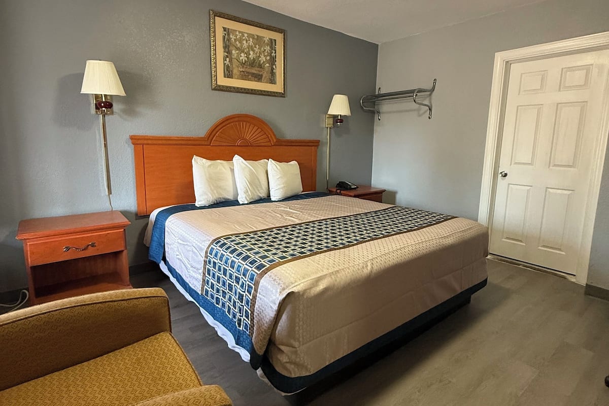 A hotel room with a bed, bedside tables, a lamp, a picture on the wall, and a door.