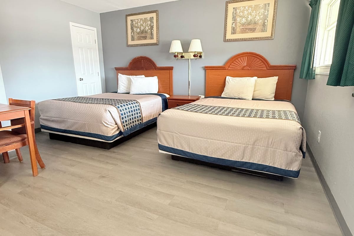 A hotel room with two beds, a desk, and a chair.