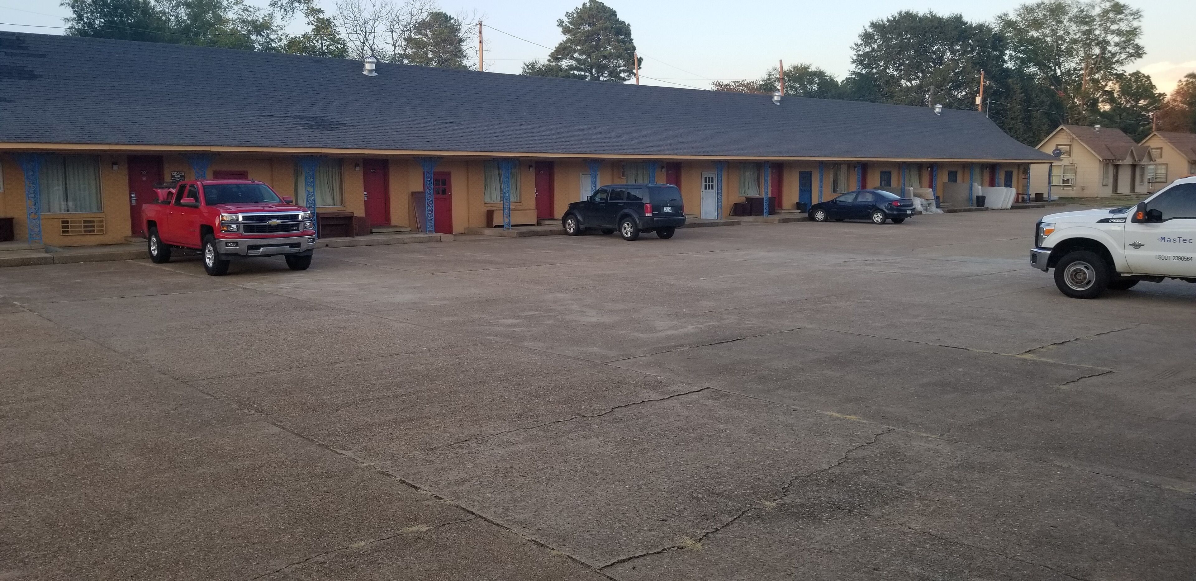Un motel avec une rangée de chambres, un parking et quelques véhicules stationnés.