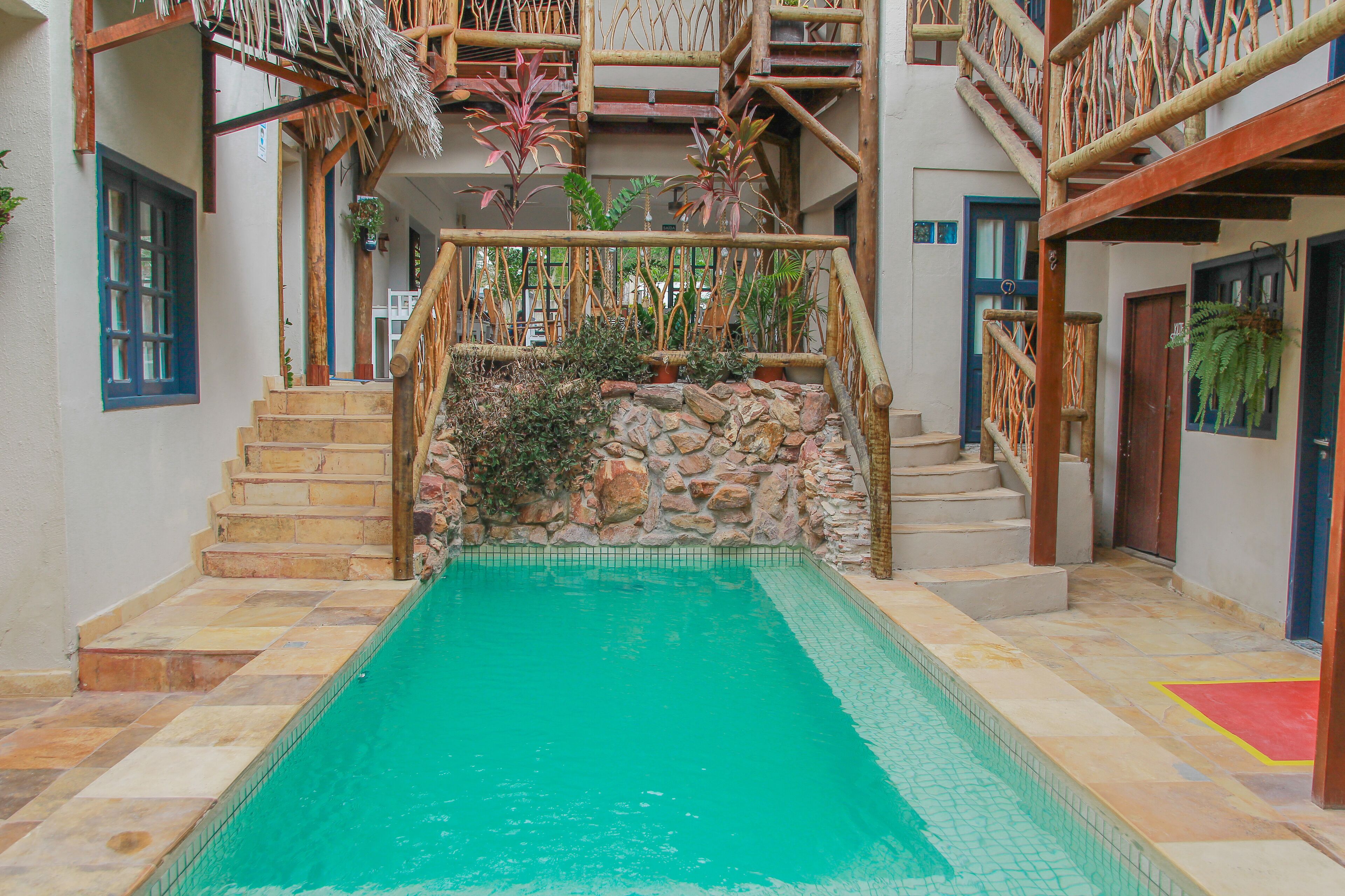 A pool area with stone steps leading to a wooden staircase, surrounded by potted plants and a stone wall.