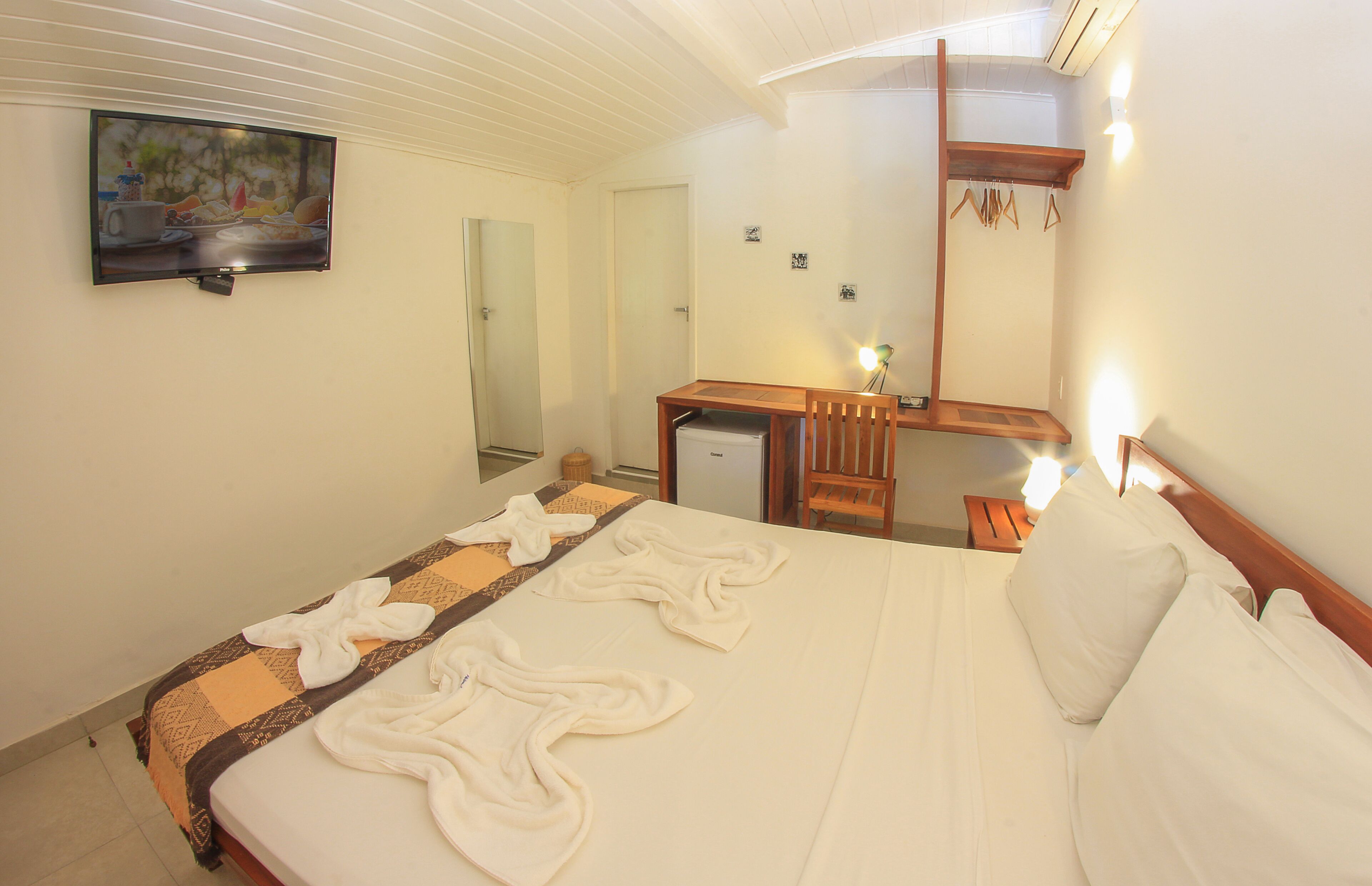 A hotel room with a bed, a desk, a mirror, and a television on the wall.