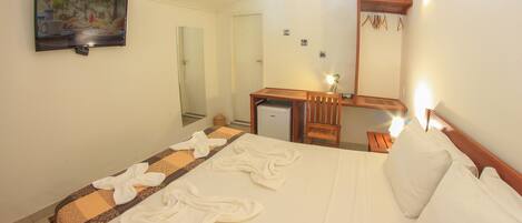 A hotel room with a bed, a desk, a mirror, and a television on the wall.