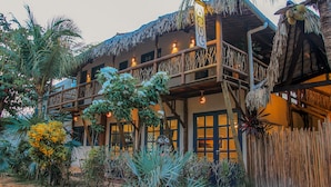 Un edificio tradicional con techo de paja, balcones de madera y una variedad de plantas tropicales.