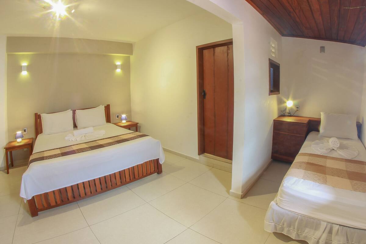 A hotel room with a large bed, a smaller bed, a wooden wardrobe, and a nightstand with a lamp.