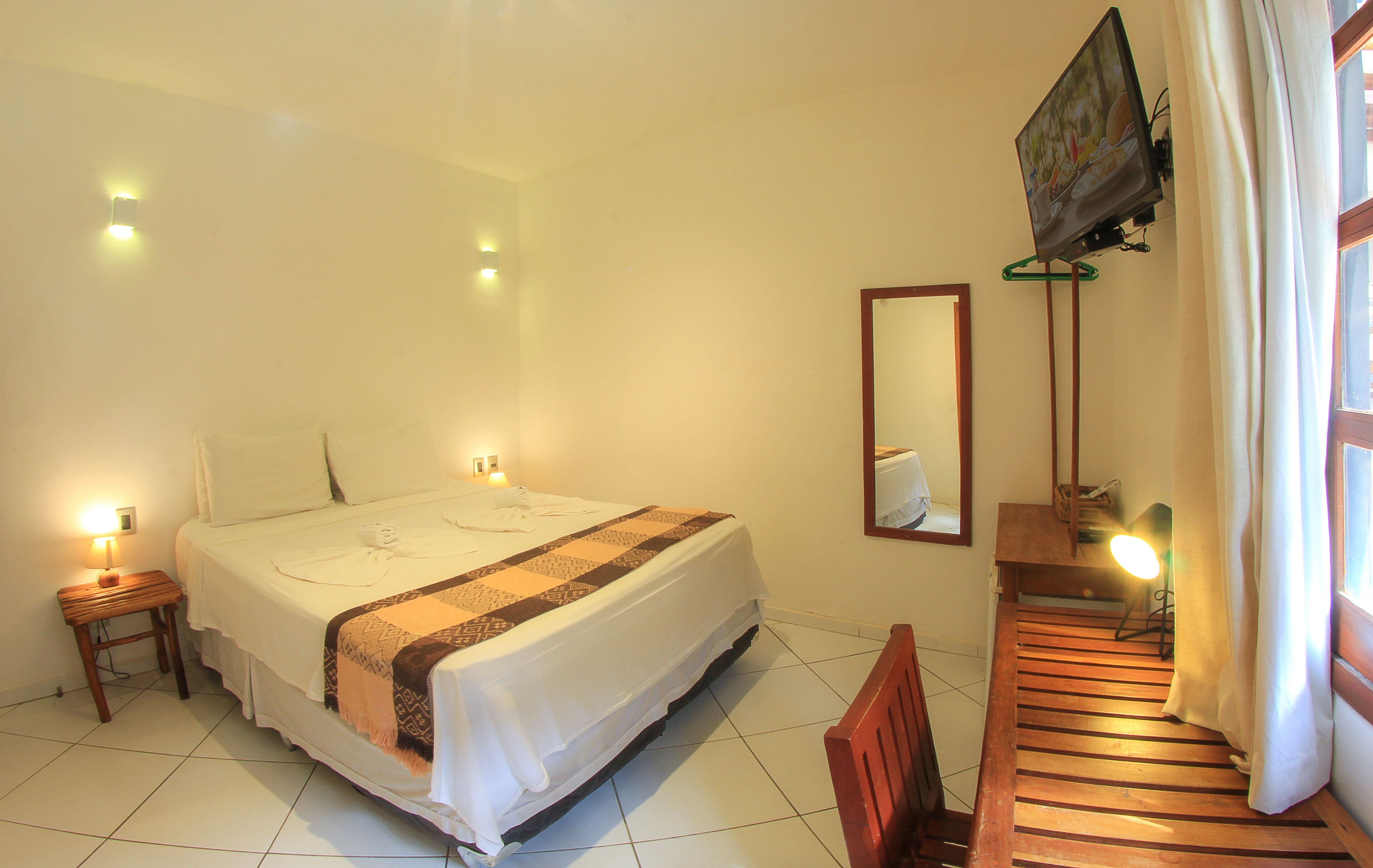 A hotel room with a bed, bedside lamps, a TV mounted on the wall, and a window with curtains.