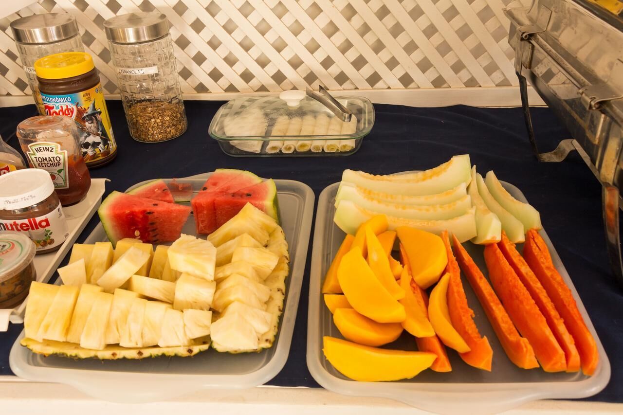 Una mesa con diferentes alimentos, incluyendo sandía, piña, mango y zanahorias, junto con condimentos como kétchup Heinz y Nutella.