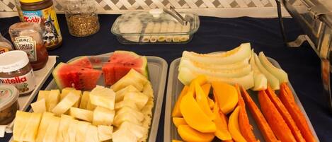 Una mesa con diferentes alimentos, incluyendo sandía, piña, mango y zanahorias, junto con condimentos como kétchup Heinz y Nutella.